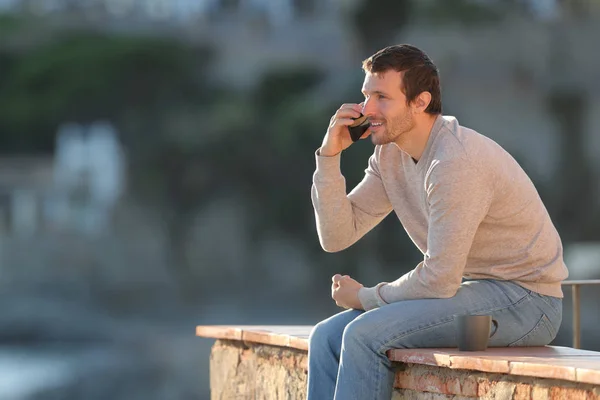 Uomo felice chiama sul cellulare seduto su un muro — Foto Stock