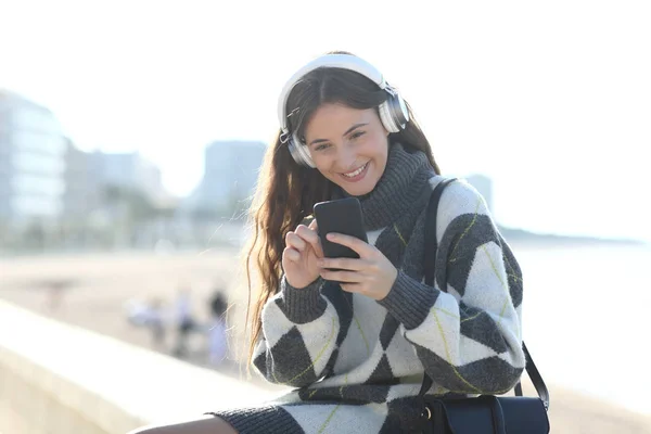 Glad flicka lyssnar på musik checkar telefon på vintern — Stockfoto