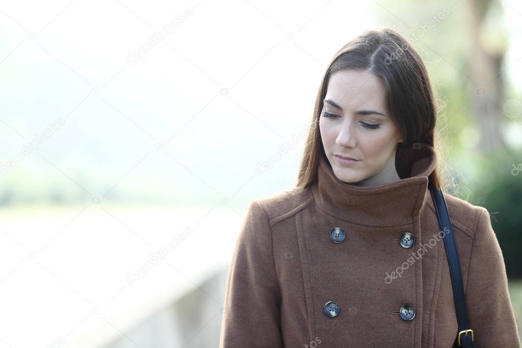 Sad woman walking alone in a park looking down