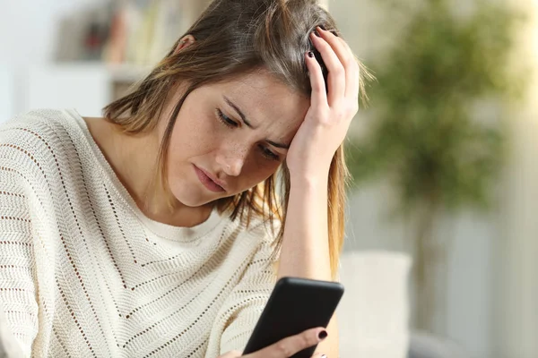 Förvirrad kvinna kontrollerar mobiltelefonen hemma — Stockfoto