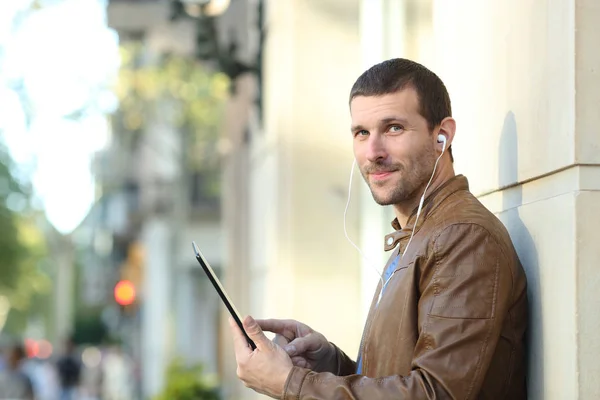 Homem usando fones de ouvido segura tablet e olha para você — Fotografia de Stock