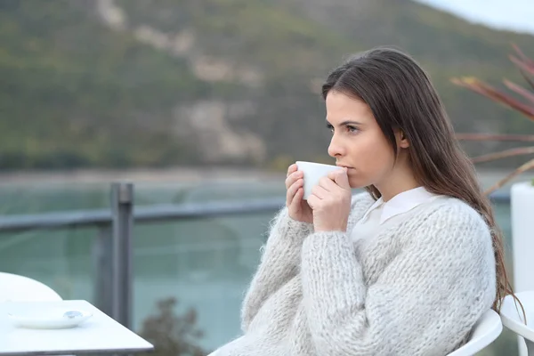 Allvarlig flicka dricker kaffe tittar bort på en terrass — Stockfoto
