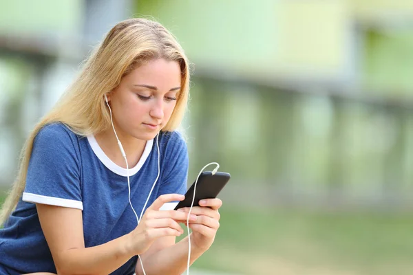 Serious teenage girl listening to music checks phone — Stock Photo, Image