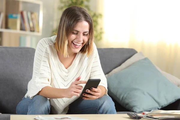 Счастливая женщина проверяет мобильный телефон дома — стоковое фото