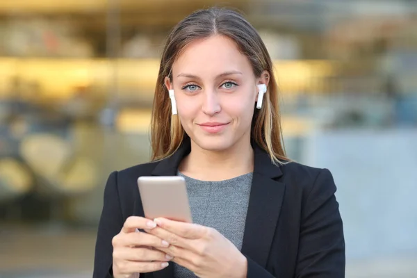Executivo usando fones de ouvido detém telefone e olha para você — Fotografia de Stock