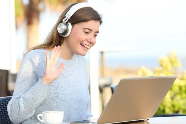 Terasta dizüstü bilgisayardaki video görüşmesi sırasında mutlu bir kız selamlaması.