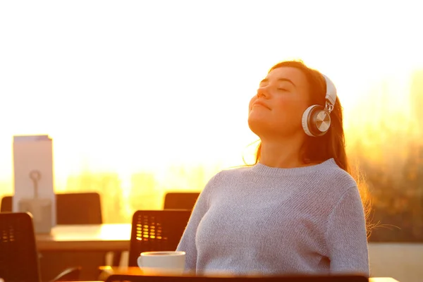 Nyugodt lány zenét hallgat a teraszon naplementekor. — Stock Fotó