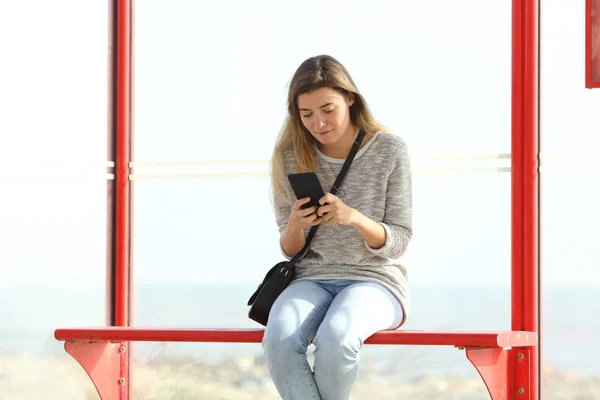 Menina verificando informações de telefone celular em uma parada de ônibus — Fotografia de Stock