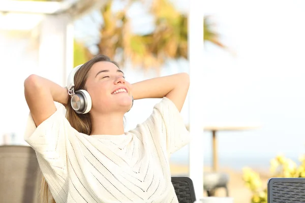 Chica feliz escuchando música descansando en una terraza en la playa — Foto de Stock