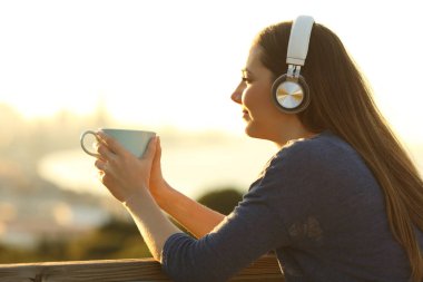 Girl relaxing with a coffee cup listening to music looking away