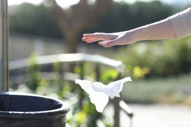 Hand throwing litter outside a bin in a park