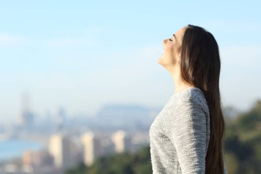 Happy woman breathing fresh air with a city in the background