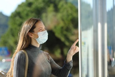 Woman wearing a mask checking schedule in a bus stop