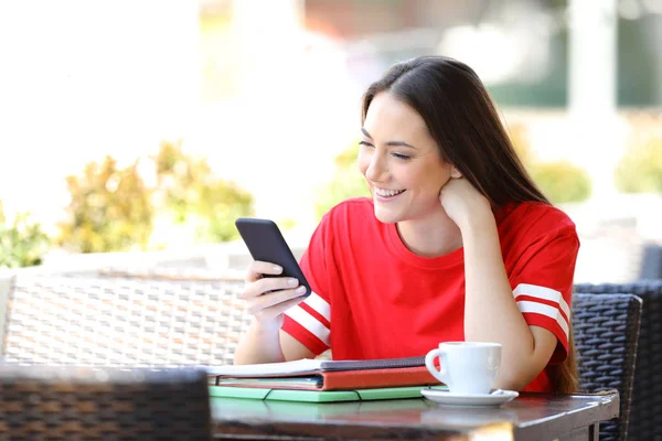 Happy student reading phone content in a coffee shop — Stockfoto