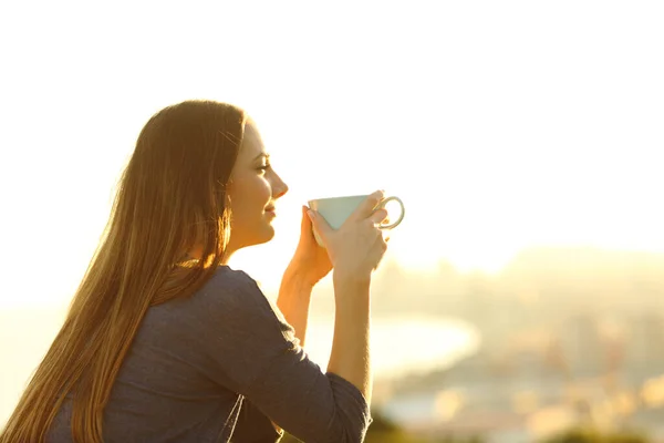 Mujer contemplando puesta de sol sosteniendo taza de café — Foto de Stock