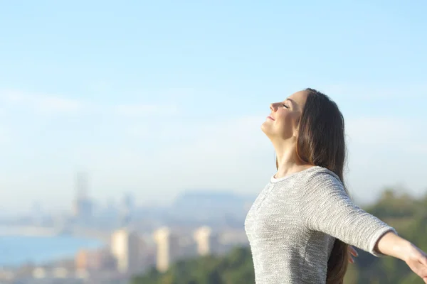 Mujer respira aire fresco con una ciudad en el fondo — Foto de Stock