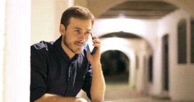 Gecenin bir yarısı sokakta oturan mutlu adam cep telefonuyla konuşuyor.