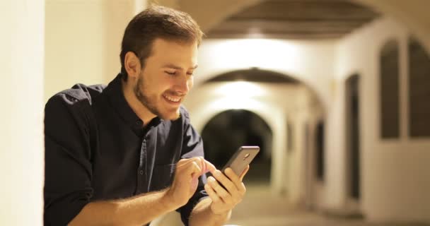 Feliz Hombre Utiliza Teléfono Inteligente Sentado Noche Calle Una Ciudad — Vídeo de stock
