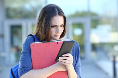 Üzgün öğrenci. Akıllı telefonu kontrol ediyor. Üniversite kampüsündeki kötü haberlerden şikayetçi.