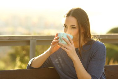 Gün batımında parkta bir bankta oturup kahve içen rahat bir kadın.