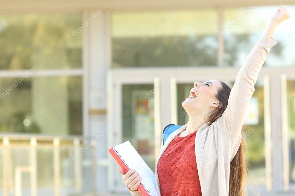 Excited student celebrating good grades raising arms standing in a college