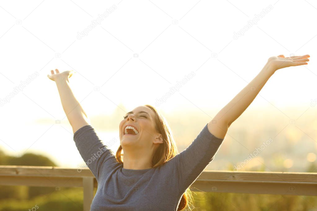 Happy woman sitting on a bench raising arms celebrating life in a park