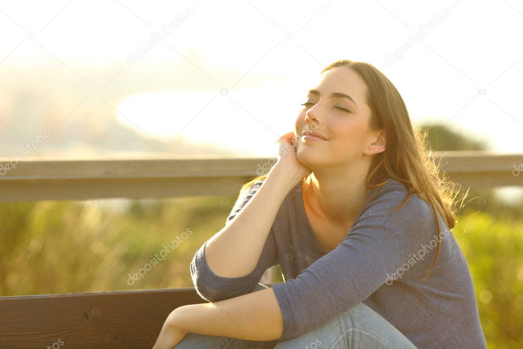 Satisfied woman relaxing sitting on a bench at sunset outdoors in city outskirts