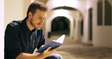 Geceleri sokakta oturup kağıt kitap okuyan mutlu bir adam.