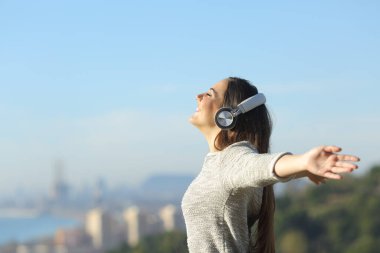 Kulaklıkla müzik dinleyen kız kollarını açıp nefes alıyor açık havada kendini özgür hissediyor.