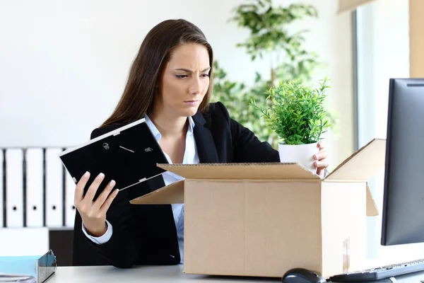 Sad fired employee boxing belongings sitting at office