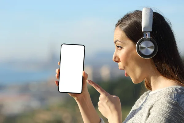 驚きの女の子のプロフィールヘッドフォンで音楽を聞きながらすごい顔をした空白のスマートフォン画面を指して — ストック写真