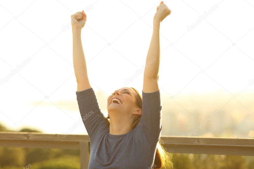Excited woman raising arms celebrating success at sunset in a park