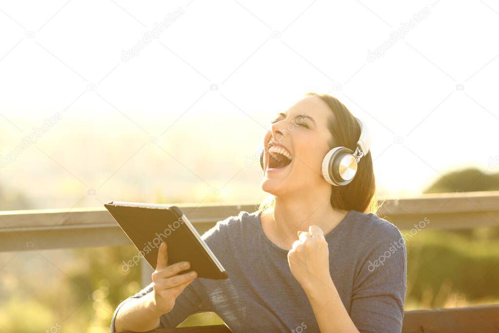 Excited woman holding a tablet and wearing headphones screaming and celebrating good news 