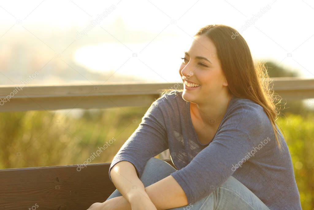 Happy woman smiling and relaxing sitted on a bench with views on the background 