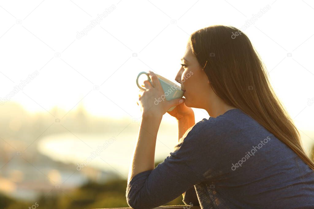 Side view portrait of a satisfied woman drinking coffee at sunset watching views from a balcony