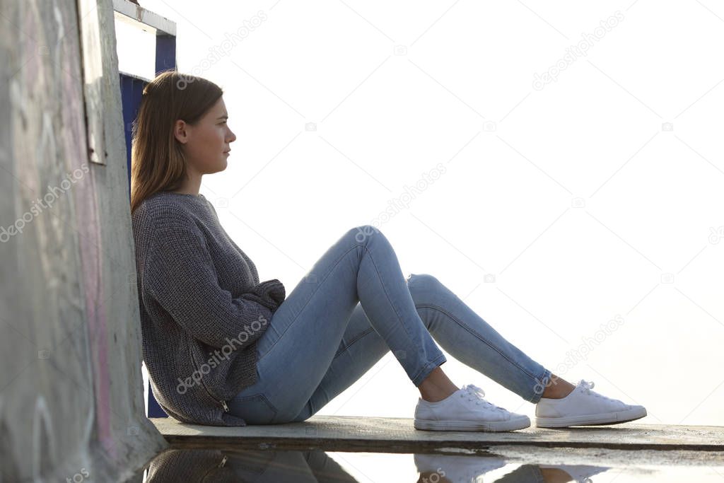 Side view portrait of a pensive teenage girl looking away sitting outdoors