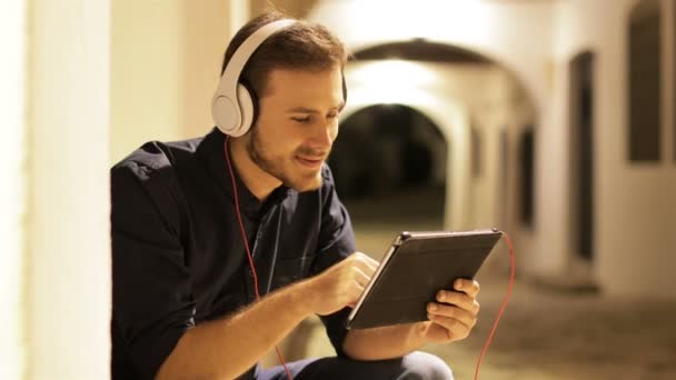 Happy Man Browsing Tablet Wearing Headphones Sitting Street Night — Stock video