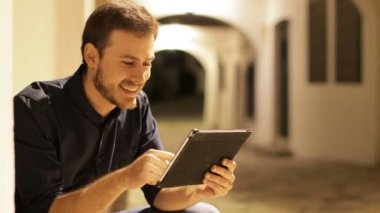 Geceleri sokakta oturup tablet okuyan mutlu bir adam.