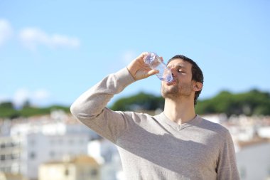 Güneşli bir günde, şehirde dikilmiş şişe su içen bir adam.