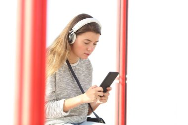 Kablosuz kulaklık takan ve otobüs durağında akıllı telefon kullanan ciddi bir genç kız.