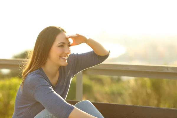 幸せな女性見て離れて手で彼女の額に座っている公園のベンチで日没 — ストック写真