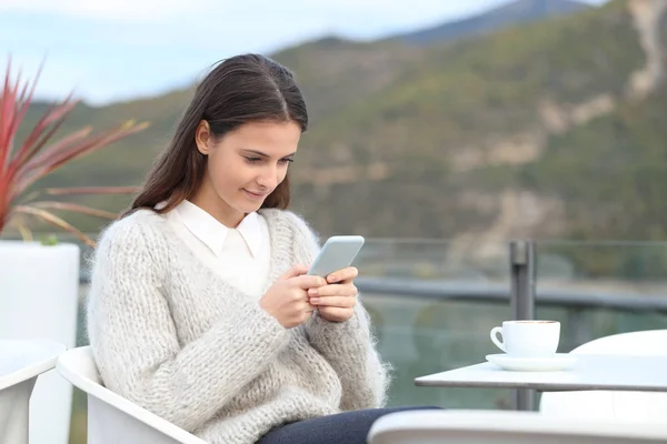 一个少女冬天在酒店阳台上检查她的智能手机的肖像 — 图库照片