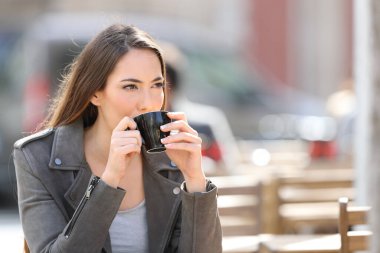 Confident young woman drinking coffee looking away sitting on a cafe terrace