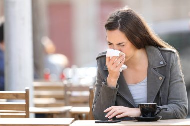 Sick woman blowing her nose with tissue sitting on a coffee shop terrace