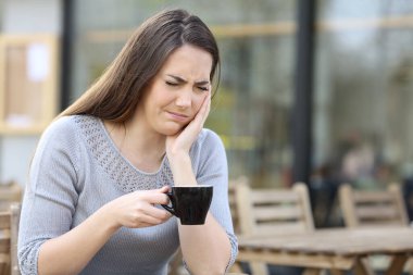 Woman suffering from painful tooth ache holding a coffee mug on a restaurant terrace