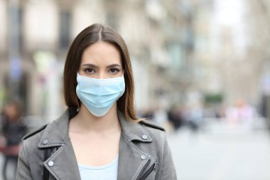 Front view portrait of serious woman with protective mask avoiding contagion looking at camera on street