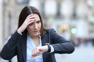 Front view of a worried business woman checking time on her smart watch on a city street