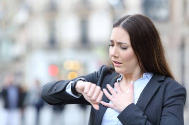 Portrait of a worried business woman holding chest checking scared her pulse on a smart watch on a city street