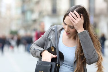 Front view of a worried woman looking preoccupied inside her bag on a city street