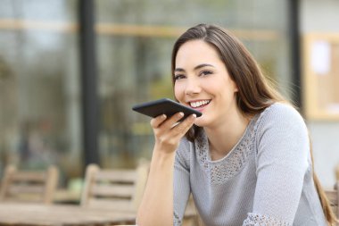 Happy woman using voice recognition system on her smart phone on a coffee shop terrace